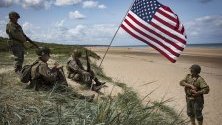 Френски ентусиасти, облечени като американски войници от Втората световна война, седят до американски флаг, засаден в пясъчна дюна на плажа Омаха на брега на Нормандия малко преди честването на 75-та годишнина на Деня на Д, който бележи началото на края на Втората световна война в Европа.