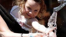 Малко момиченце се мокри с  вода на чешма в центъра на Загреб, Хърватия.
