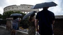 Туристи се опитват да се предпазят от дъжда с чадъри край Колизеумът в Рим, Италия.
