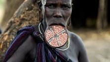 Жена от номадското племе мурси в Етиопия позира с диск в устните си. На 15-16 г. жените от племето режат долната си устна, за да вкарат в нея парче глина. С времето дупката се уголемява - колкото е по-голяма, толкова жената е смятана за по-красива.