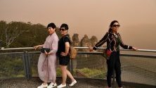 Туристи позират пред скалния феномен Трите сестри в Катумба край Сидни, Австралия. Горските пожари са пред мегаполиса.