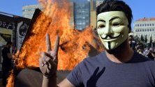 Протестиращ с маска показва знака на победата пред клада, запалена от демонстранти, блокирали път към парламента в Бейрут, Ливан. Сесията на парламента е отложена неопределено заради натиска от улицата.