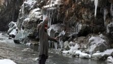 Човек се опитва да запази равновесие край замръзнал поток след рязко спадане на градусите в Кашмир, Индия.