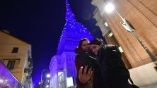 Туристи се снимат край монумента Моле Антонелиана в Торино, Италия, осветен със светлини за Коледа.