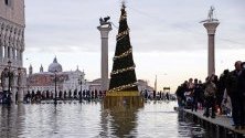 Туристи на наводнения площад &quot;Сан Марко&quot; във Венеция, на която има разположена коледна елха въпреки високата вода.