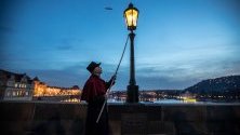 Дежурен пали лампите по Карловия мост в Прага, облечен в историческа униформа. Паленето е туристическа атракция по време на коледните праници.