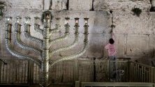Момче поставя листче с желание в Стената на плача в Ерусалим, застанало до огромна златна Менора за еврейския празник Ханука.