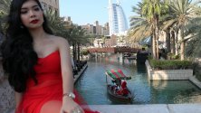 Жена позира за снимка докато мъже, облечени като Дядо Коледа, минават с лодка с туристи към селото на Дядо Коледа, а отзад се вижда луксозния небостъргач &quot;Бурж ал Араб&quot;, Дубай, ОАЕ.