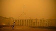 Чистач пред парламента в Канбера, Австралия, на фона на пушек от горските пожари в региона.