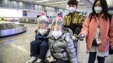 Деца носят защитни маски и импровизирана защита върху лицата си от пластмасови бутилки срещу коронавируса на летището в Гуанджоу, Китай.