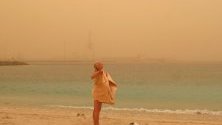 Туристка се суши след плуване на брега във Фуертавентура, Канарските острови, докато зад нея в небето се виждат облаци от прах и пясък от пустинята Сахара.