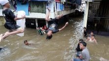 Деца скачат във водите на наводнен квартал в Джакарта, Индонезия. Проливните дъждове потопиха мегаполиса под вода, която на места достига 150 см.