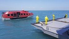 Служители в защитни костюми чакат акостирането на военен кораб-болница с пациенти, евакуирани от круизния кораб World Dream заради наличие на коронавирус. 